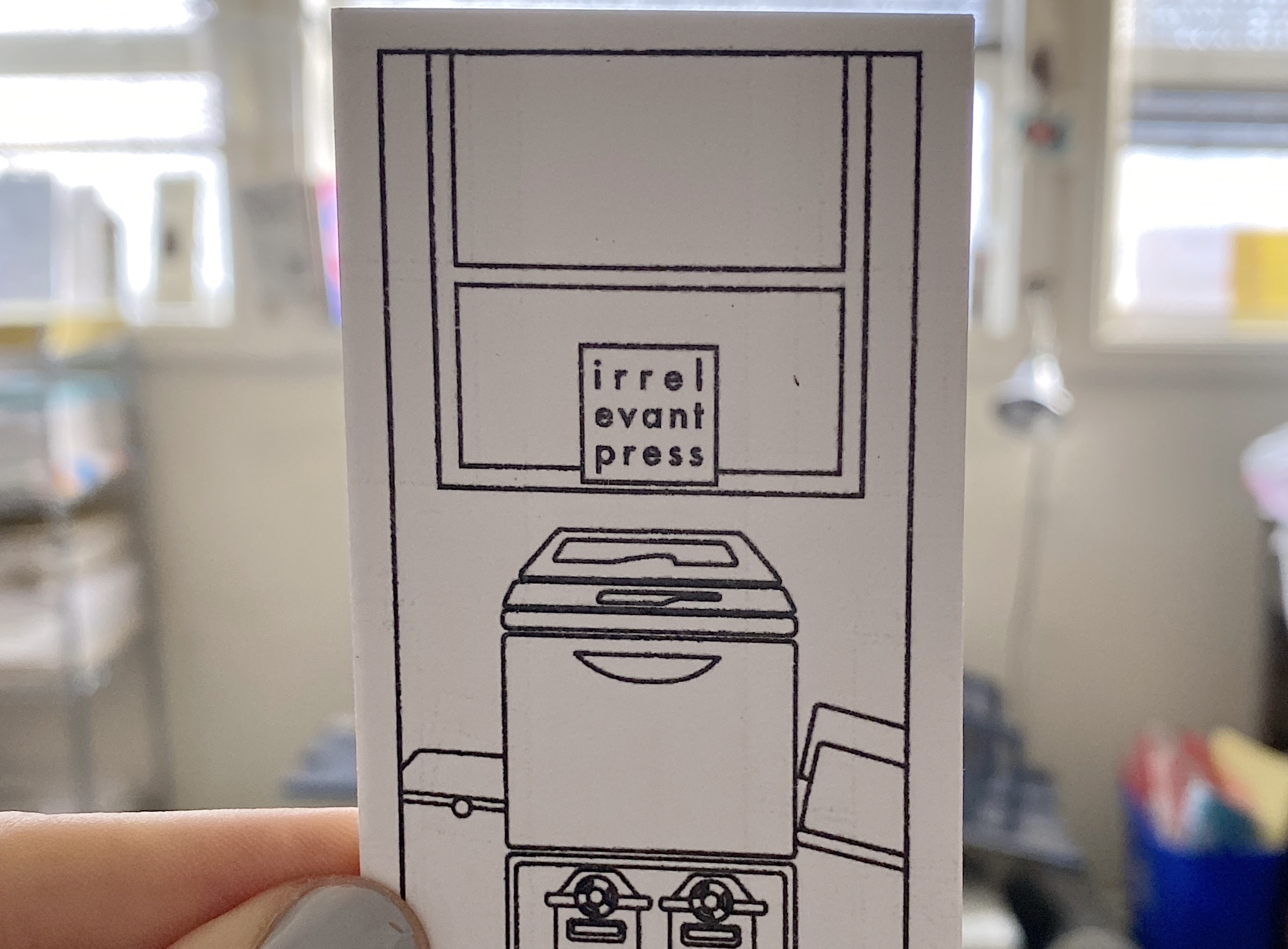 A hand holding up a rectangular piece of paper with a graphic design of a printer and a sign that reads "irrelevant press."