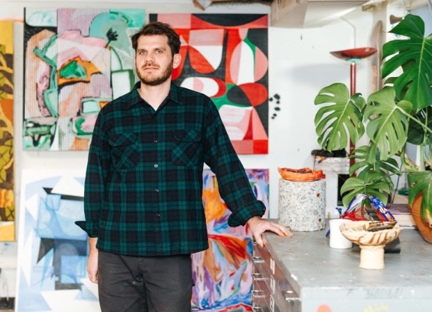 Brett Flanigan standing in a room full of colorful art and plants.