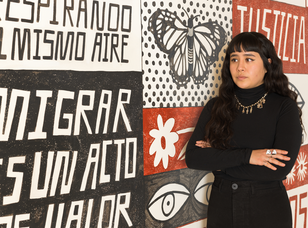 Liz Hernández standing in front of her mural "Conjuro para la sanación de nuestro futuro (A spell for the healing of our future)" at SFMOMA.