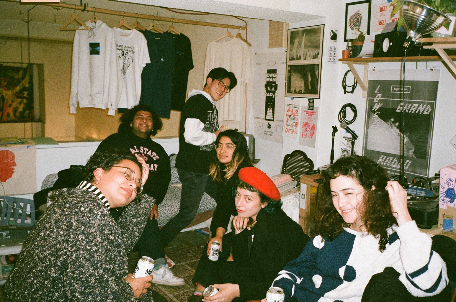 A group of people hanging out in a casual room with posters on the wall and a record player in the corner.