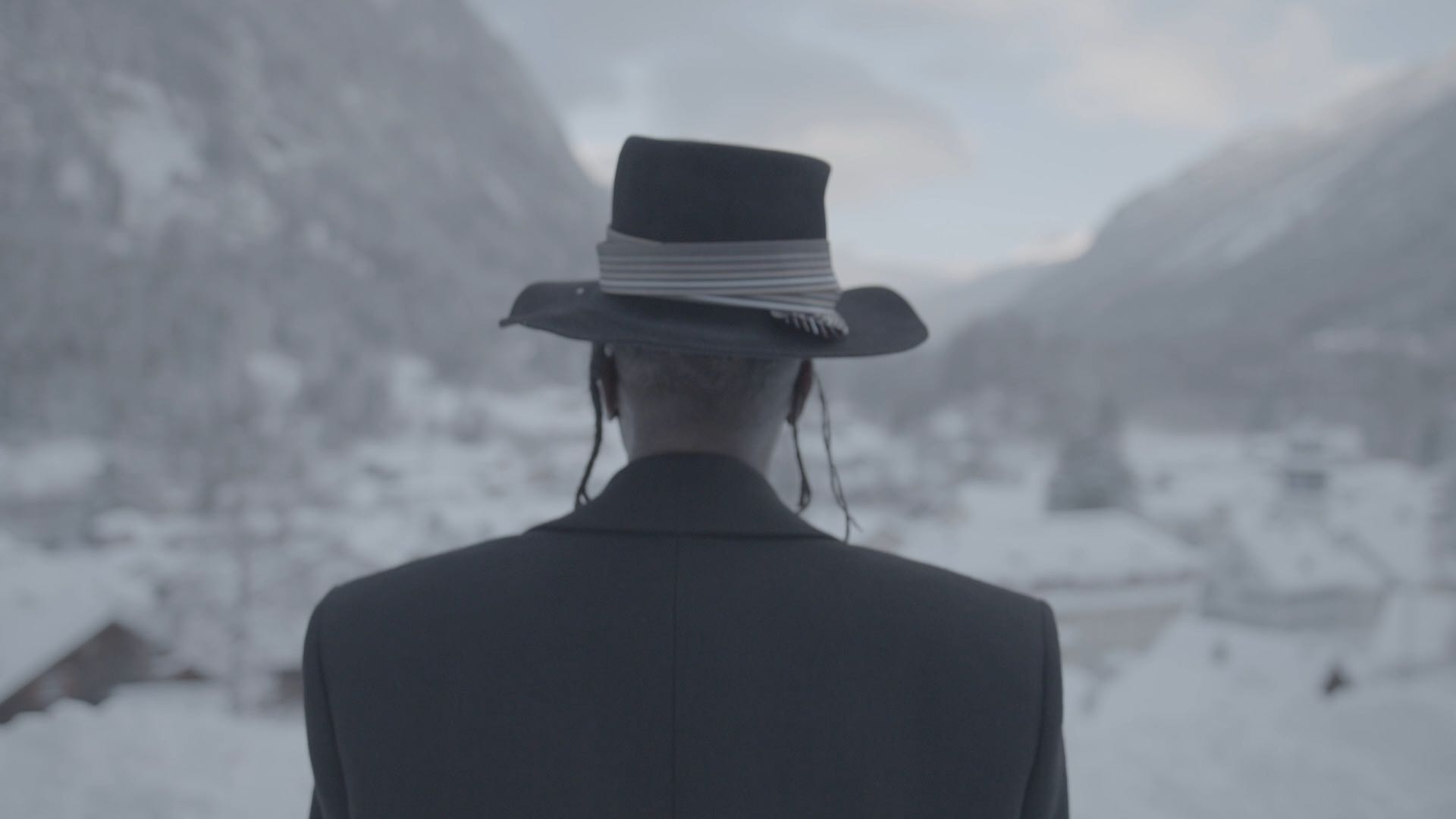 A person standing with their back to the viewer as they look out on a snowy mountain scene.