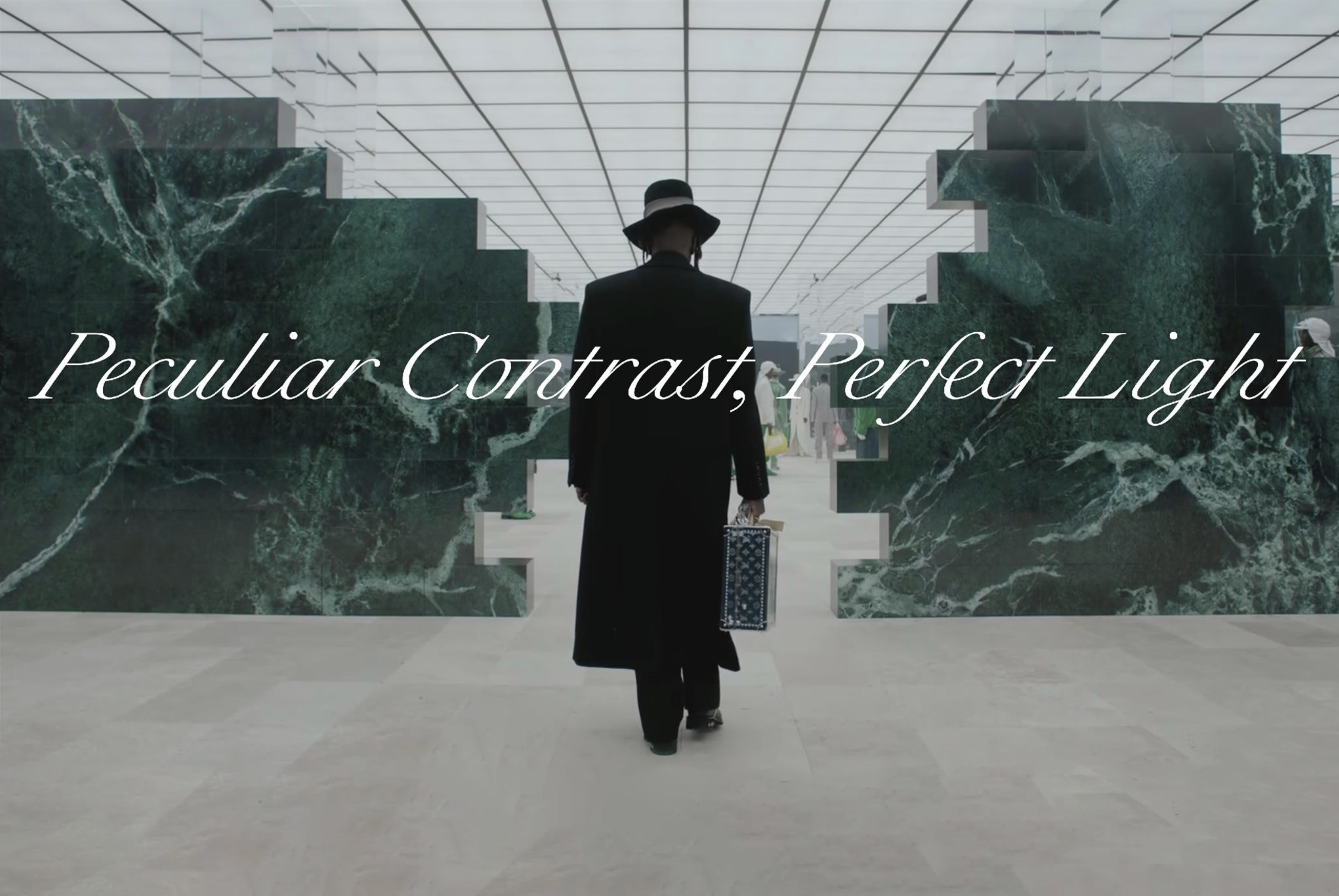 Film still of a person walking away from the viewer into a large room with artistic marble wall dividers overlaid with the words "Peculiar Contrast, Perfect Light."