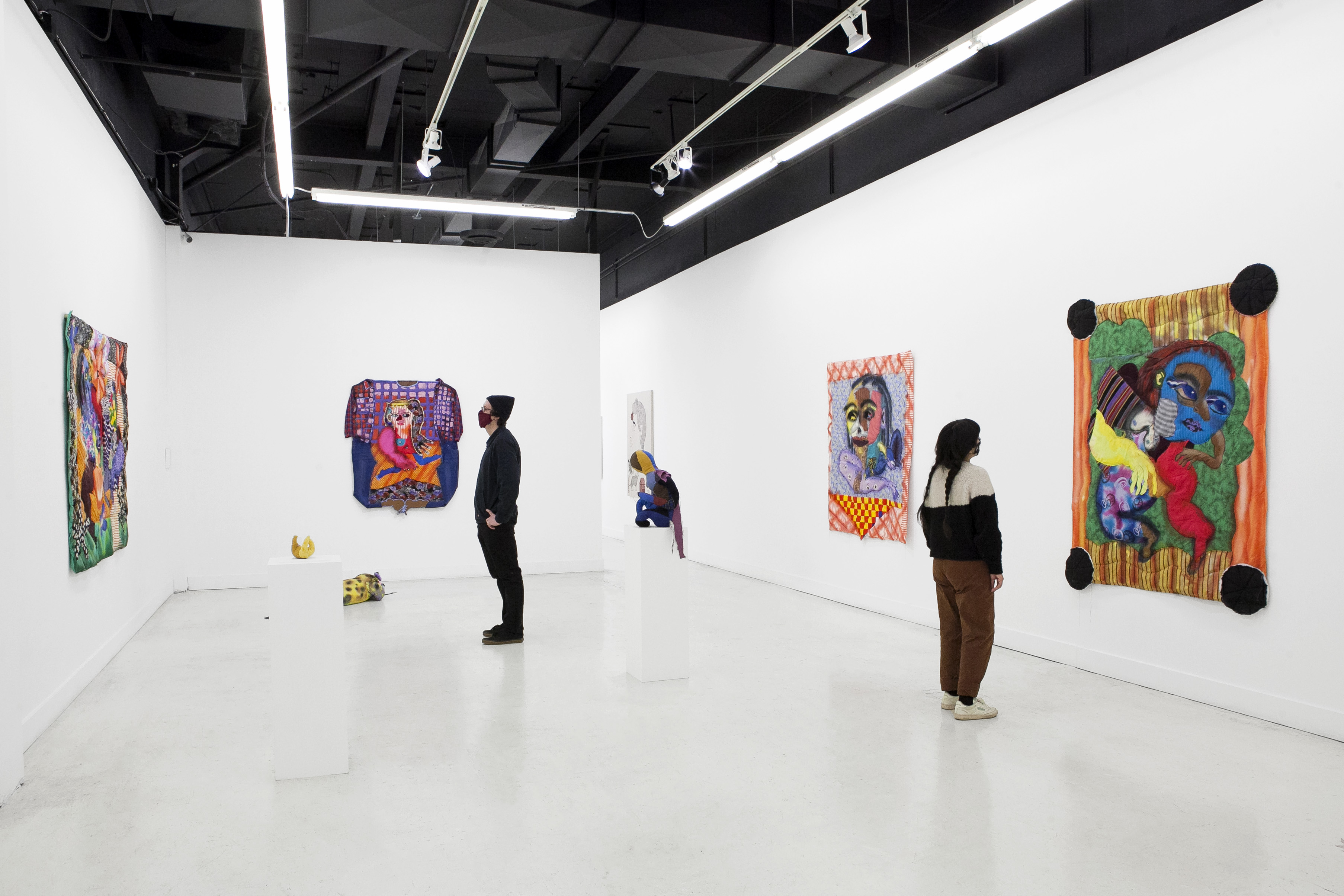 Two people standing in pt. 2 Gallery looking large colorful paintings.