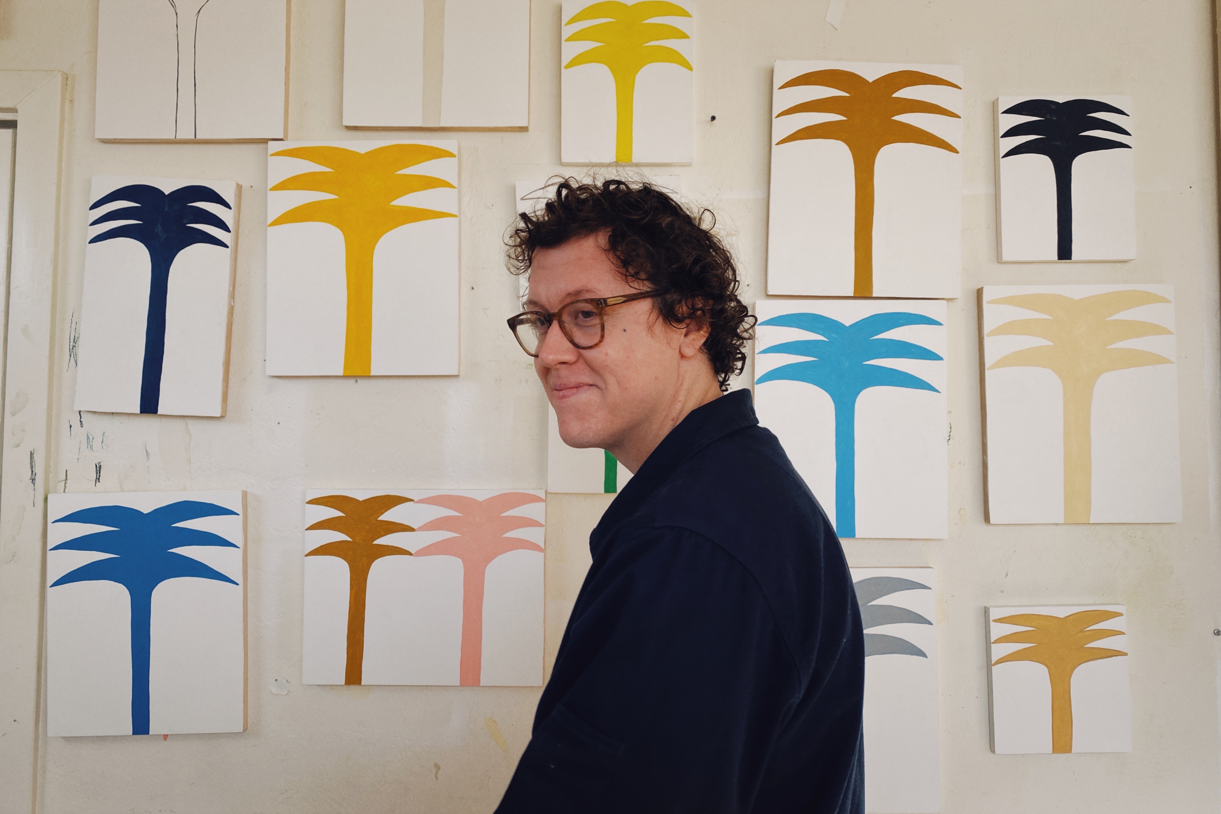 Ryan Whelan standing sideways in front of various colored graphic representations of palm trees.